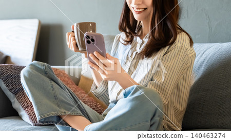 A woman sitting on a sofa in the living room and using a smartphone A woman sitting on a sofa in the living room and using a smartphone 140463274