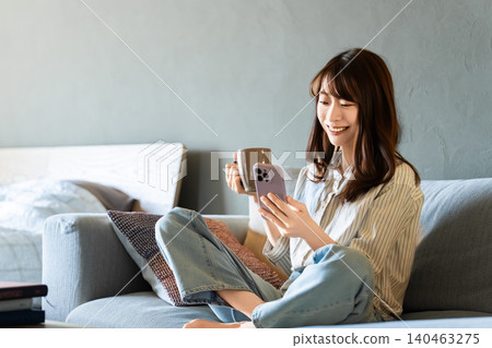 一位女士坐在客廳的沙發上,正在使用智慧型手機 一位女士坐在客廳的沙發上,正在使用智慧型手機 140463275