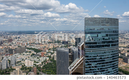 Expansive vista over Moscow reveals a mix of contemporary buildings, lush green spaces, and a vibrant city alive under a clear blue sky during summer. 140463573
