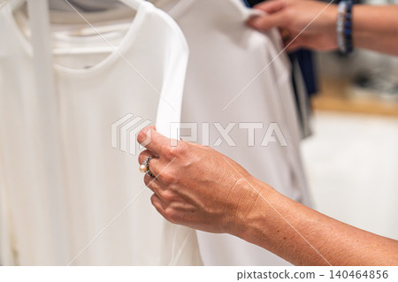 Woman shopping for white blouses, selecting and inspecting garments on a clothing store rack Woman shopping for white blouses, selecting and inspecting garments on a clothing store rack 140464856