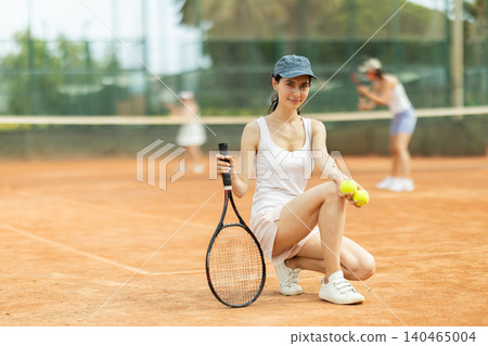 Woman in sportswear against backdrop of outdoor tennis court Woman in sportswear against backdrop of outdoor tennis court 140465004
