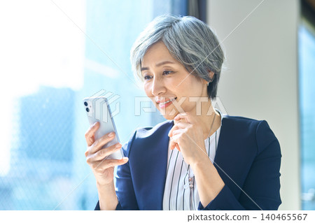 A gray-haired woman thinking while looking at her smartphone A gray-haired woman thinking while looking at her smartphone 140465567
