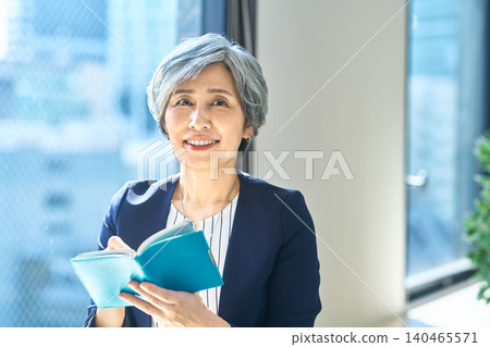 A gray-haired woman opens her notebook and looks up. A gray-haired woman opens her notebook and looks up. 140465571