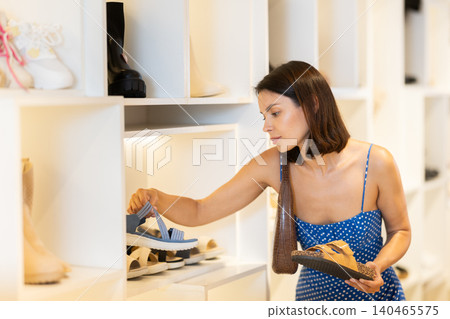 Girl customer chooses sandals in store, and buyer carefully examines product. Girl customer chooses sandals in store, and buyer carefully examines product. 140465575