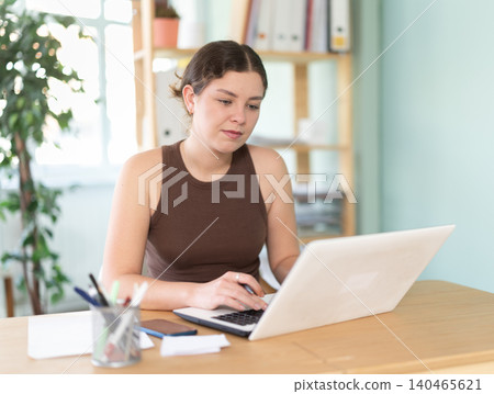 woman is sitting at a desk in an office and typing on a laptop woman is sitting at a desk in an office and typing on a laptop 140465621