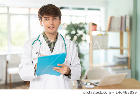 Young male doctor writing notes in paper folder in medical clinic Young male doctor writing notes in paper folder in medical clinic 140465859