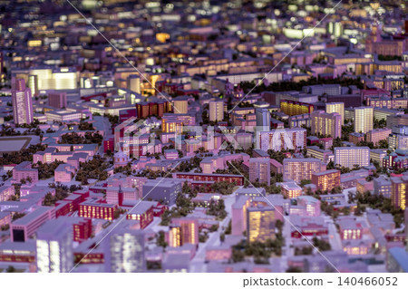 A vibrant miniature model of a city features intricate buildings, illuminated windows, and winding streets, capturing the essence of urban life at dusk. 140466052