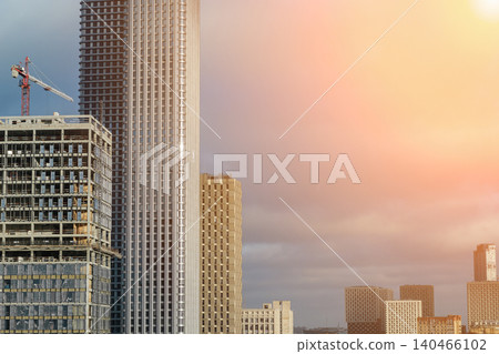 Several tall buildings are under construction in a city as the sun sets, creating an urban landscape with cranes and modern structures. Several tall buildings are under construction in a city as the sun sets, creating an urban landscape with cranes and modern structures. 140466102