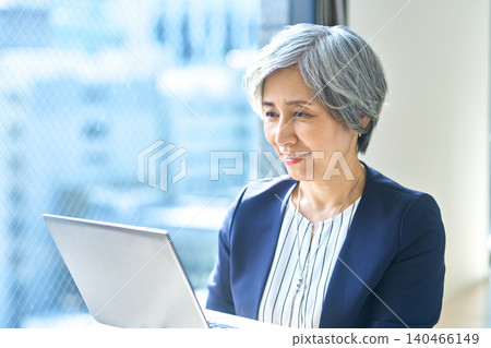A woman smiling while looking at her PC by the window. A woman smiling while looking at her PC by the window. 140466149