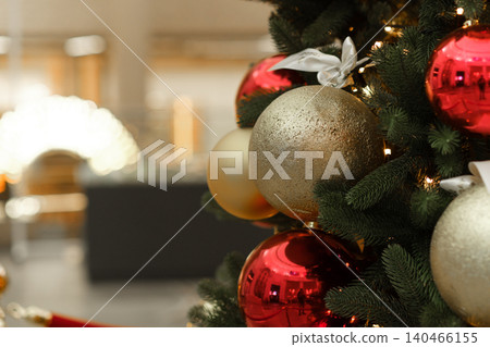 A Christmas tree stands in a shopping mall, adorned with red and gold ornaments, creating a festive atmosphere for holiday shoppers. 140466155