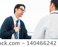 A male patient in a tie complains of chest pain and discomfort to a doctor in a hospital examination room. 140466242