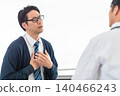 A male patient in a tie complains of chest pain and discomfort to a doctor in a hospital examination room. 140466243