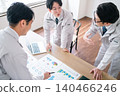 Three male office workers in work clothes are seen smiling and chatting while looking at documents in a conference room. 140466246