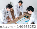 Three male office workers in work clothes are seen smiling and chatting while looking at documents in a conference room. 140466252