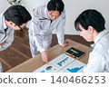 Three male office workers in work clothes are seen smiling and chatting while looking at documents in a conference room. 140466253