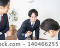 Businessmen in suits sit around a desk in the room, discussing while using documents and laptops. 140466255