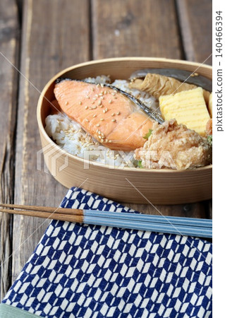 A Japanese bento box containing grilled salmon in a bentwood container, wrapped in a cloth with a Yagasuri (arrow feather) pattern. 140466394