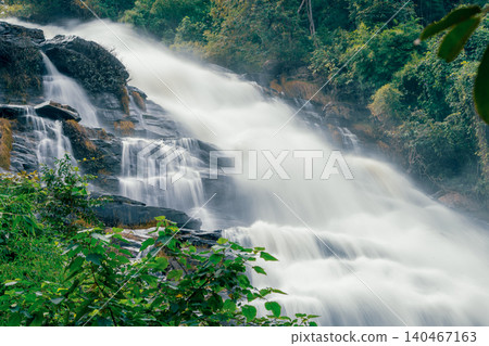 Beautiful waterfall with a lush green forest in the background. The water is flowing down the rocks and creating a beautiful scene. Sustainable waterfall in lush forest promoting water sustainability. 140467163