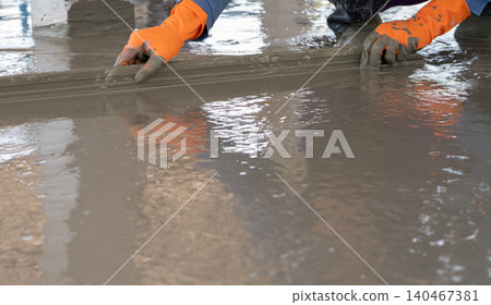 Mason worker working with trowel to level cement floor at construction site. A skilled construction worker spreading wet concrete to level wet concrete on a site floor. Foundation and flooring tasks. Mason worker working with trowel to level cement floor at construction site. A skilled construction worker spreading wet concrete to level wet concrete on a site floor. Foundation and flooring tasks. 140467381