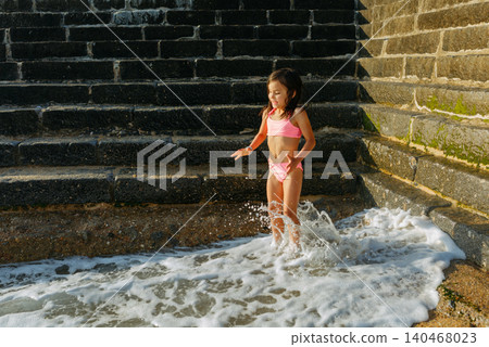 happy small girl jumping in the waves next to the wall happy small girl jumping in the waves next to the wall 140468023
