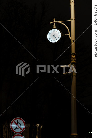 Clock shows the time at night on a street pole with signs indicating no strollers and no bicycles in the area. Clock shows the time at night on a street pole with signs indicating no strollers and no bicycles in the area. 140468278