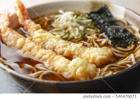 A warm bowl of tempura soba noodles with two large shrimp tempura pieces, served in a black bowl, garnished with seaweed and green onions. A warm bowl of tempura soba noodles with two large shrimp tempura pieces, served in a black bowl, garnished with seaweed and green onions. 140470071