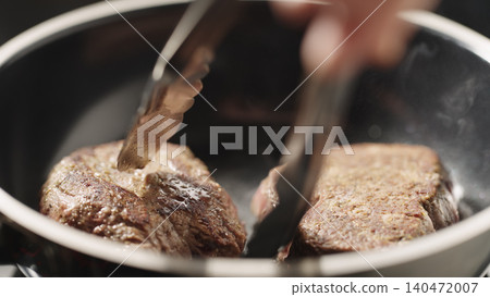 Seared beef fillets sizzling in a frying pan with tongs lifting one piece Seared beef fillets sizzling in a frying pan with tongs lifting one piece 140472007