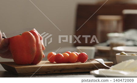 Close-up of red bell pepper being sliced on wooden cutting board with cherry tomatoes Close-up of red bell pepper being sliced on wooden cutting board with cherry tomatoes 140472009