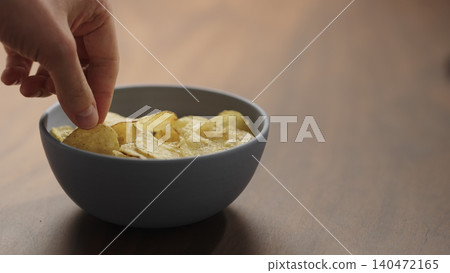 Close-up of man hand take potato chips in a ceramic bowl on wooden table 140472165