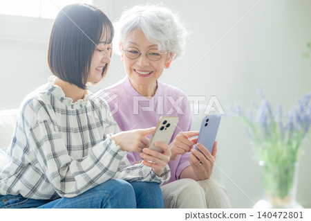 A senior woman looking at her smartphone and her grandchild A senior woman looking at her smartphone and her grandchild 140472801