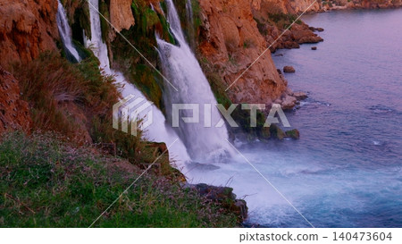 Waterfall cascading into ocean from red cliff at dusk Waterfall cascading into ocean from red cliff at dusk 140473604
