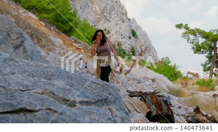 Woman hiker walking rocky mountain trail with steep limestone cliffs Woman hiker walking rocky mountain trail with steep limestone cliffs 140473641