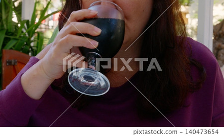 Woman drinking dark beverage from black glass outdoors Woman drinking dark beverage from black glass outdoors 140473654