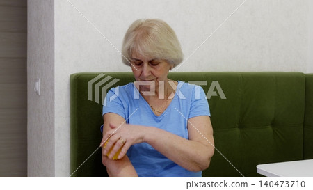 Senior woman examining arm skin on green sofa at home 140473710