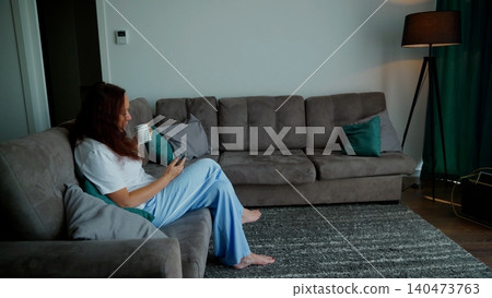 Woman relaxing on gray couch drinking water in modern living room Woman relaxing on gray couch drinking water in modern living room 140473763