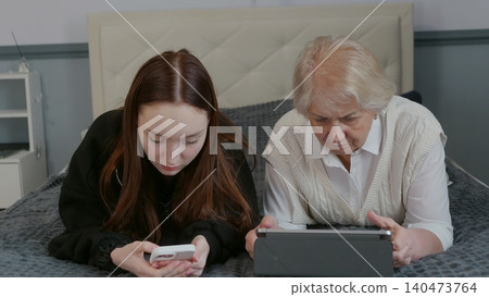 Senior woman, teenage girl using tablet together on bed Senior woman, teenage girl using tablet together on bed 140473764
