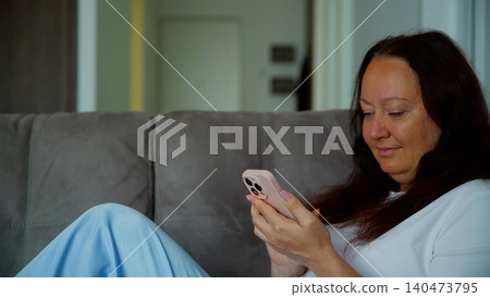 Woman relaxing on couch using smartphone at home Woman relaxing on couch using smartphone at home 140473795