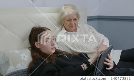 Senior woman, teen girl viewing tablet together on couch Senior woman, teen girl viewing tablet together on couch 140473851