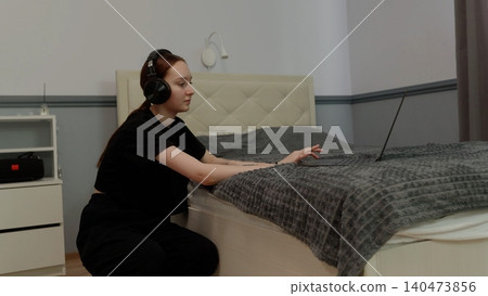 Woman wearing headphones dancing on bedroom bed Woman wearing headphones dancing on bedroom bed 140473856