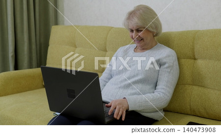Senior woman using laptop on yellow sofa at home Senior woman using laptop on yellow sofa at home 140473908