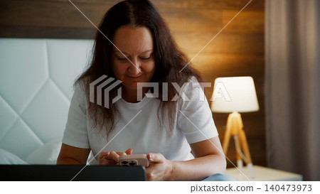 Woman relaxing at home using smartphone by warm lamp light Woman relaxing at home using smartphone by warm lamp light 140473973