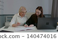 Senior woman, young girl writing notes together at desk with laptop 140474016
