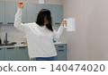 Woman celebrating with raised fist holding coffee mug in modern kitchen 140474020