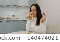 Woman drinking juice, eating bread in kitchen 140474021