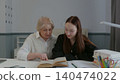 Senior woman mentoring teenage girl reading textbook together at desk 140474022
