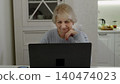 Senior woman using laptop at home kitchen table 140474023