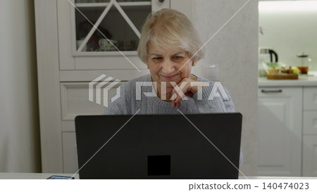 Senior woman using laptop at home kitchen table Senior woman using laptop at home kitchen table 140474023
