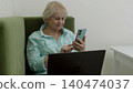 Senior woman using smartphone while working on laptop 140474037