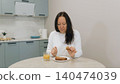 Woman eating sandwich with juice at kitchen table 140474039
