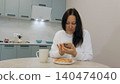 Woman using smartphone during breakfast in modern kitchen 140474040